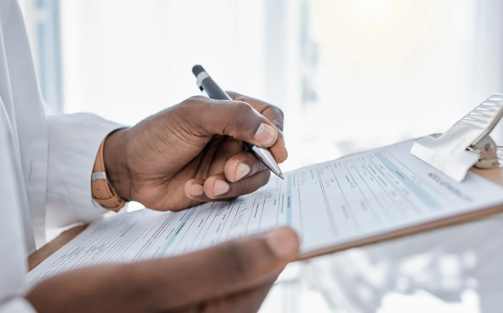 Hand completing insurance paperwork on a clipboard at a medical office